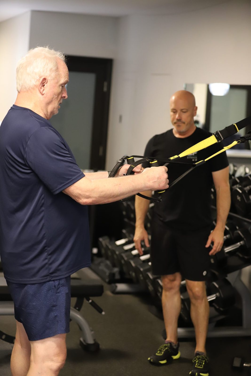 An Executive Fitness trainer coaching an older client through a suspension-strap row.